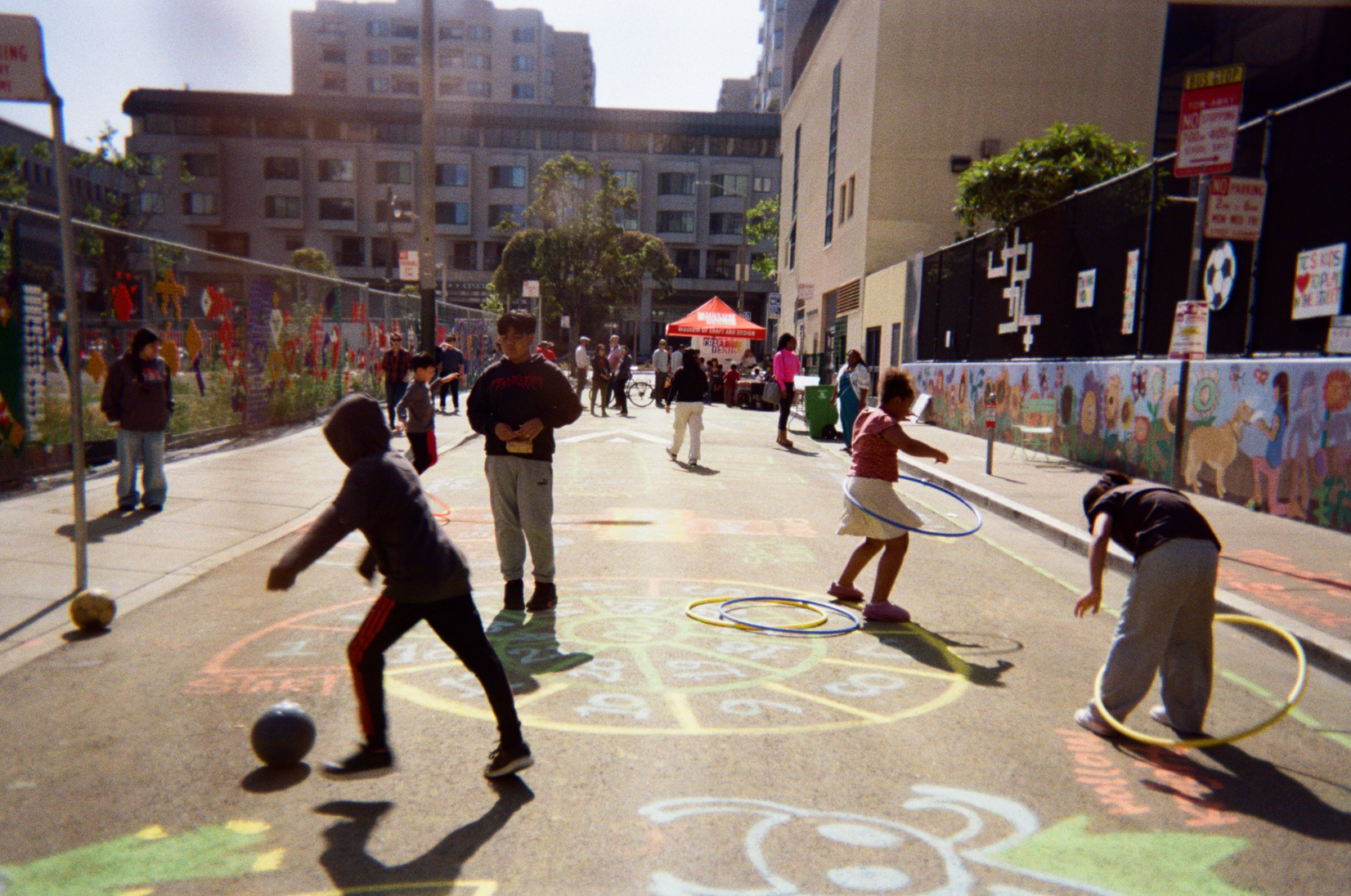 Children playing hopscotch and hula-hooping on a painted living sidewalk in San Francisco